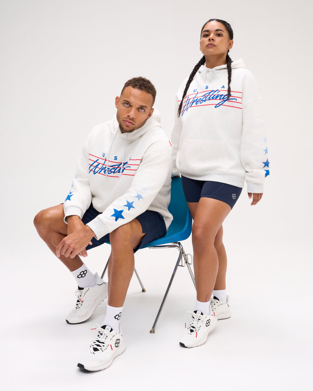 Male and female models wearing the RUDIS USA Wrestling Star Relaxed Comfort Fleece Hoodie in Heather Silver, featuring blue USA Wrestling script, red stripes and blue star sleeve graphics.