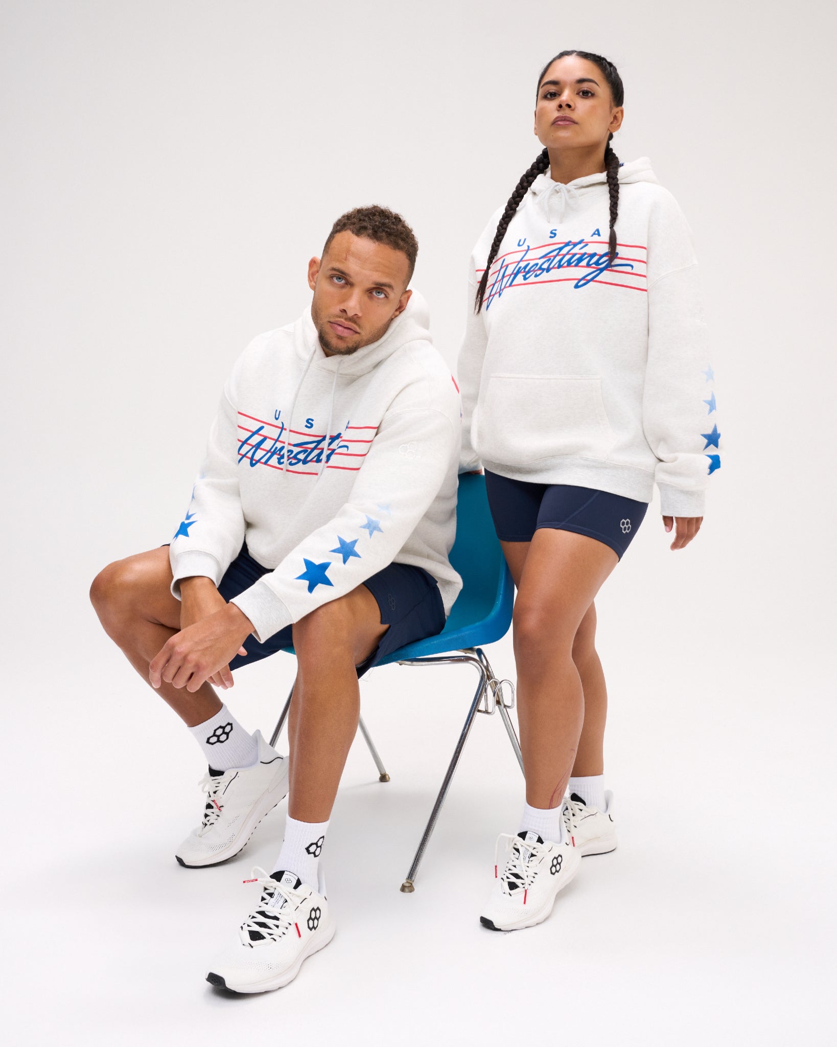 Male and female models wearing the RUDIS USA Wrestling Star Relaxed Comfort Fleece Hoodie in Heather Silver, featuring blue USA Wrestling script, red stripes and blue star sleeve graphics.