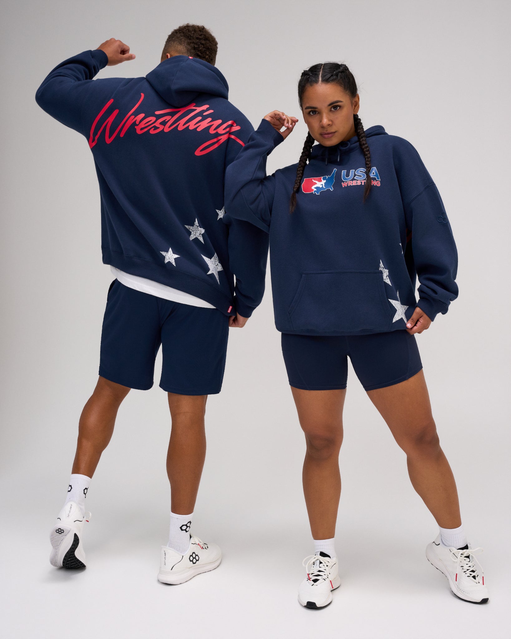 Male and female models wearing the RUDIS USA Wrestling Script Relaxed Comfort Fleece Hoodie in Navy, showing the USA Wrestling chest logo, red Wrestling back script and white star graphics.