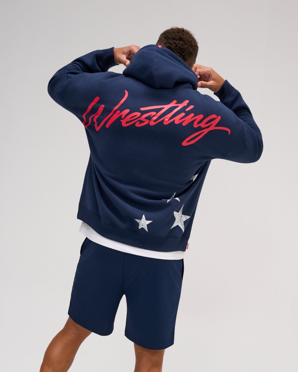 Back view of the RUDIS USA Wrestling Script Relaxed Comfort Fleece Hoodie in Navy, featuring oversized red Wrestling script across the shoulders and distressed white stars near the hem.