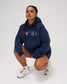Female model wearing the RUDIS USA Wrestling Script Relaxed Comfort Fleece Hoodie in Navy, featuring a red, white and blue USA Wrestling chest logo, drawstring hood and relaxed fit.