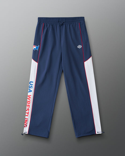 Front view of the RUDIS USA Wrestling Movement Podium Pants in navy, featuring white side panels, red piping, USA Wrestling graphics, RUDIS logo, and adjustable ankle cords.