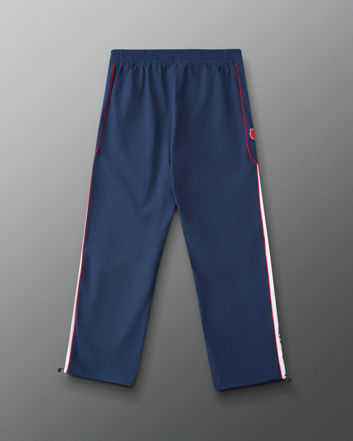 A pair of navy blue athletic pants with white and red side stripes, shown flat against a gray gradient background.