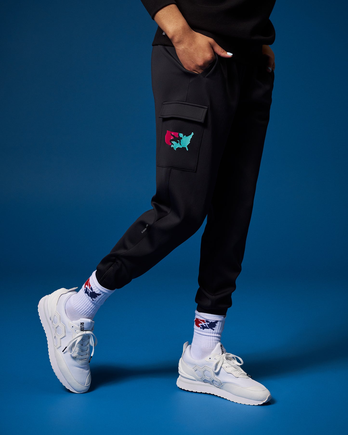 Person wearing black cargo pants with colorful patches on a blue background