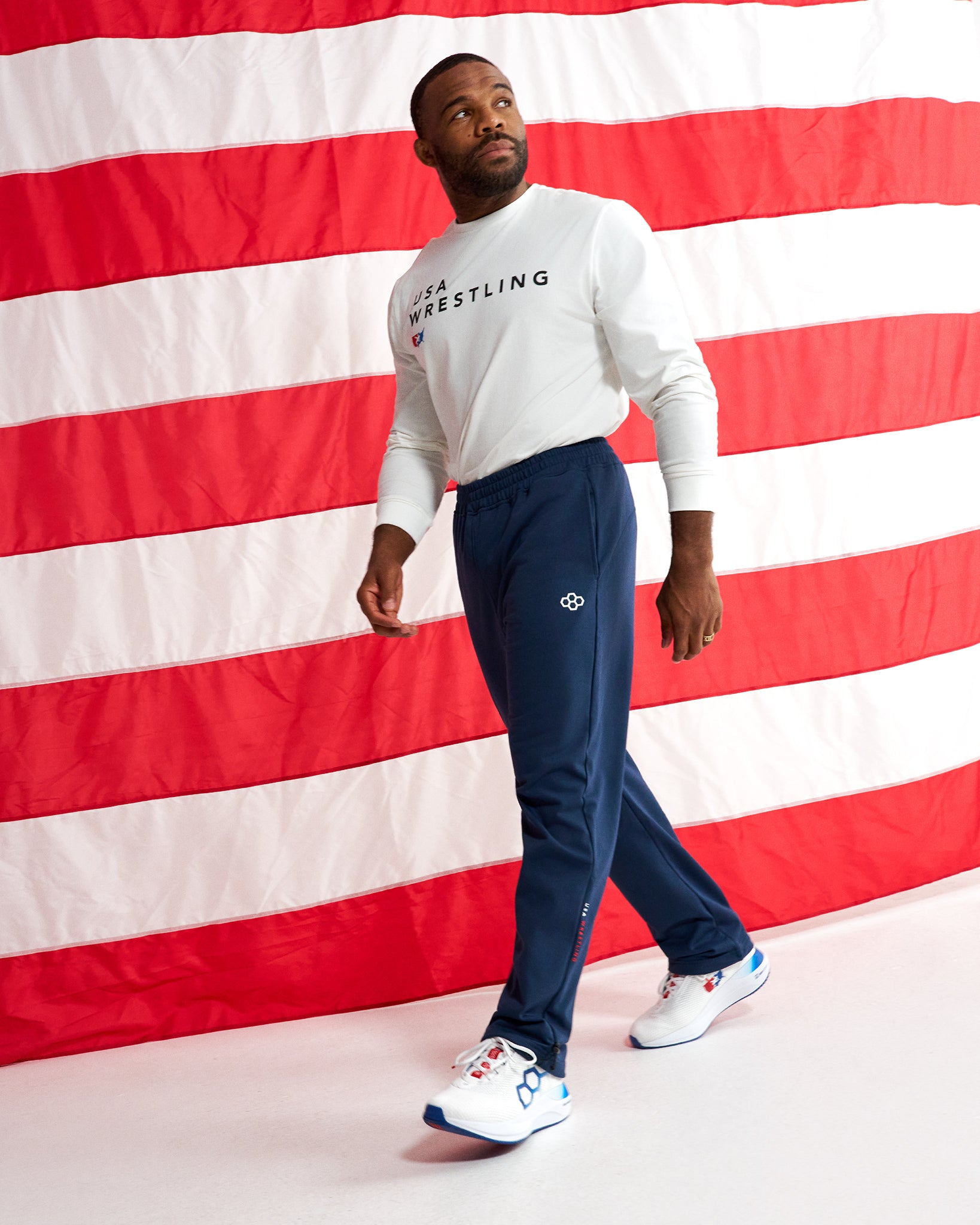 RUDIS USA Wrestling Luxe Terry Jogger in Navy worn with a USA Wrestling long sleeve shirt and training shoes in front of an American flag.