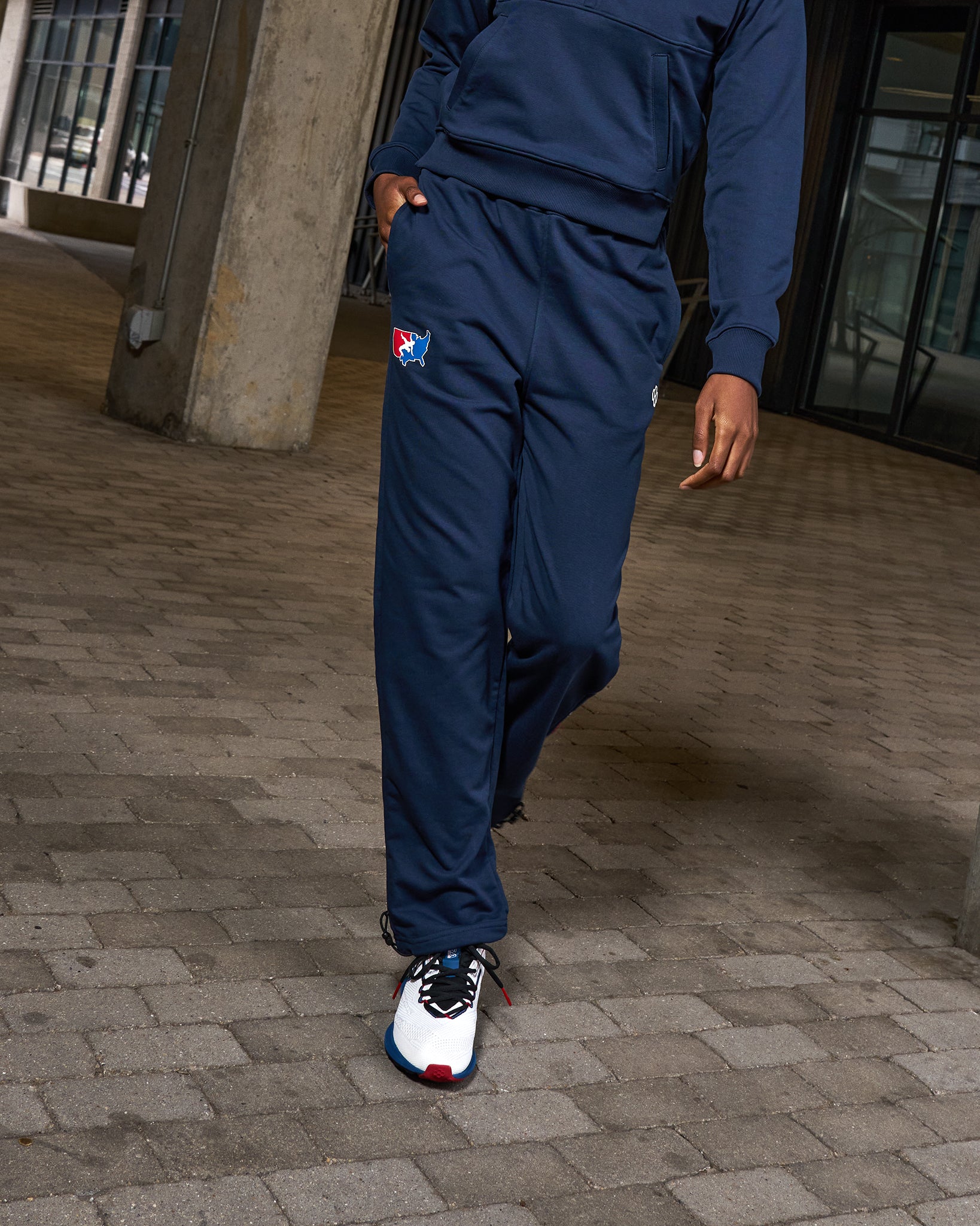 Person wearing a blue tracksuit with a logo on a paved ground.