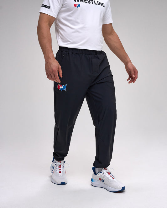 Person wearing a white t-shirt with 'Wrestling' text, black pants with a 'USA Wrestling' logo, and white sneakers on a gray background