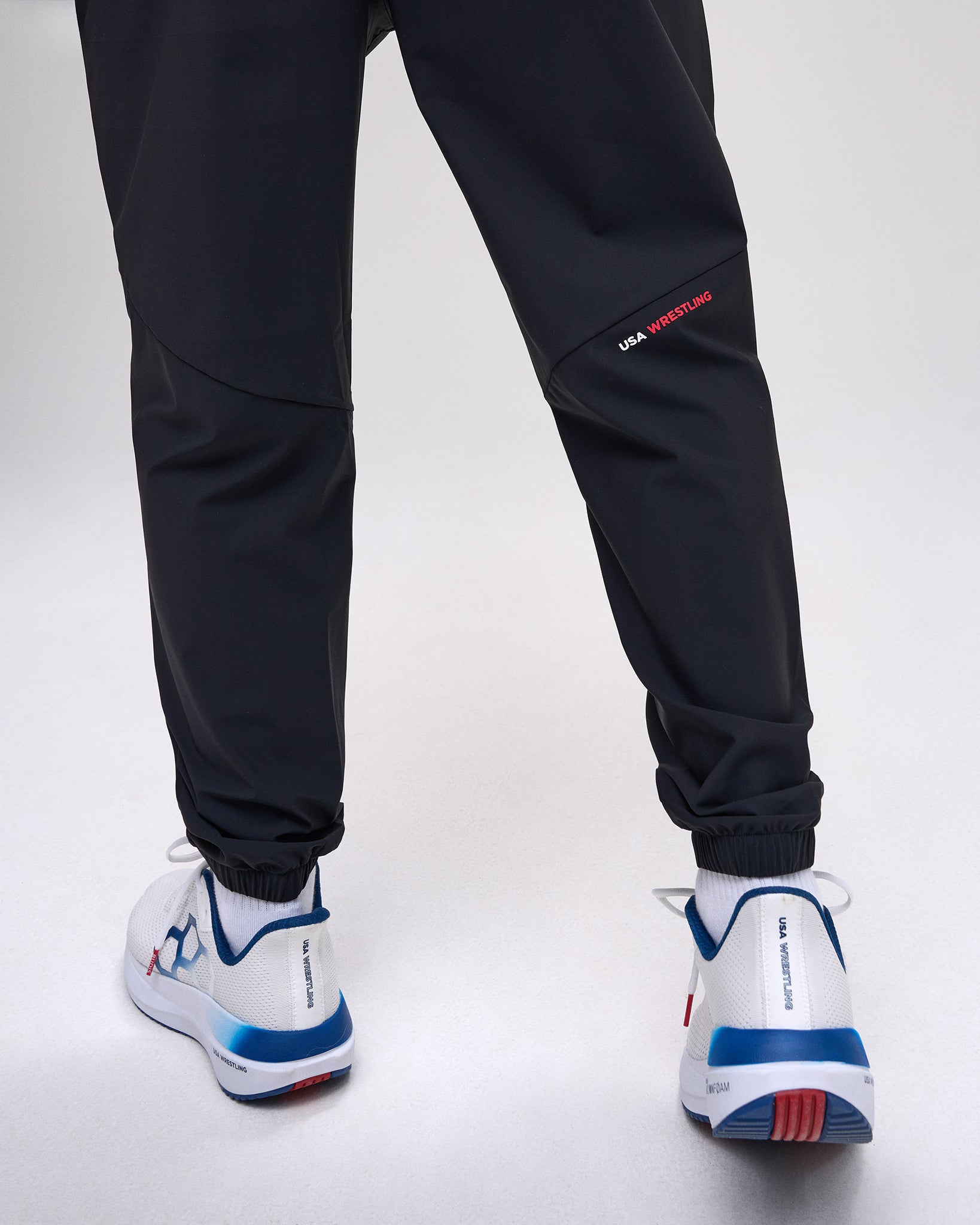 Black pants with red and white accents worn with white sneakers on a white background