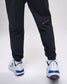 Black pants with red and white accents worn with white sneakers on a white background