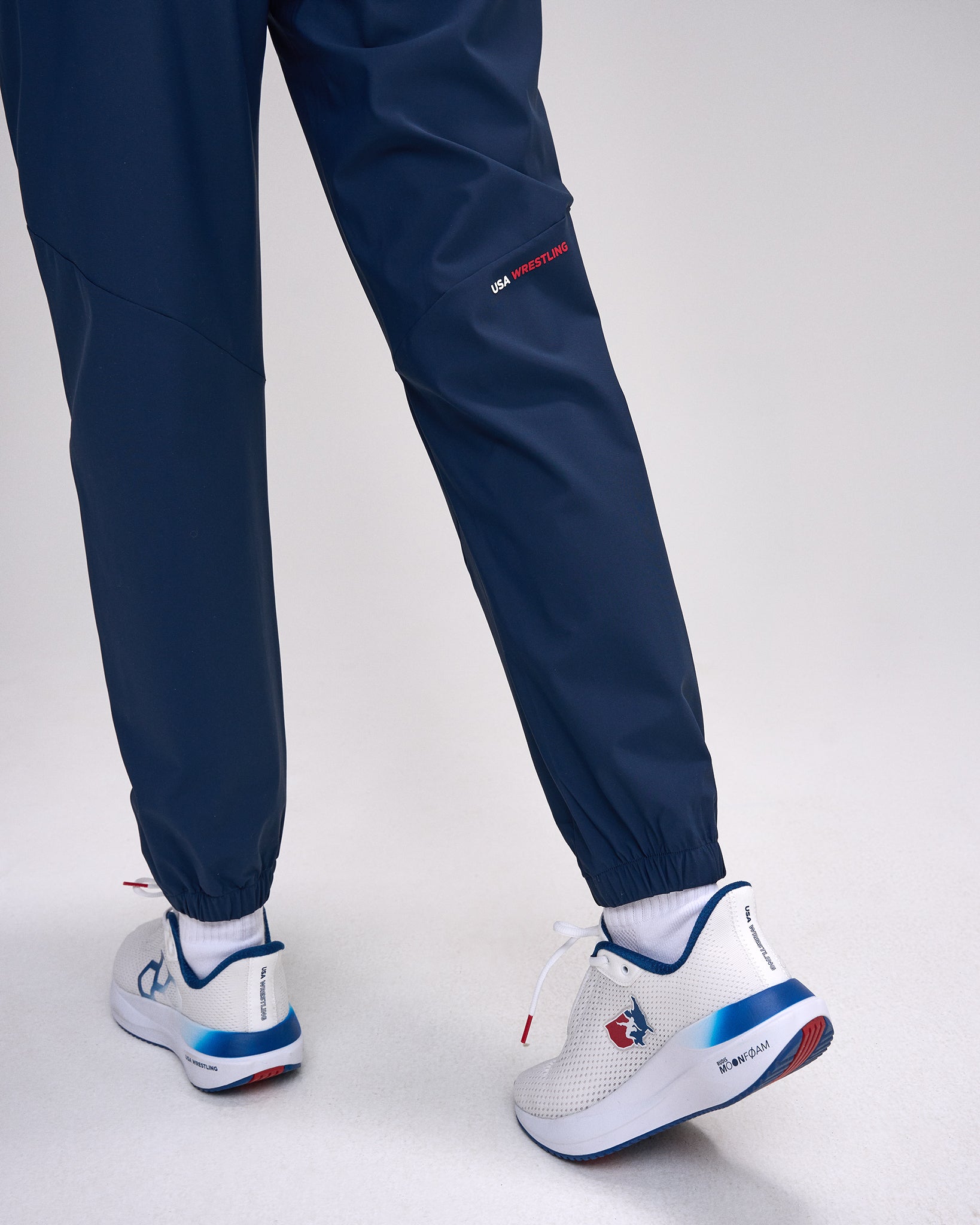 Navy tracksuit pants and white sneakers with blue and red accents on a light gray background
