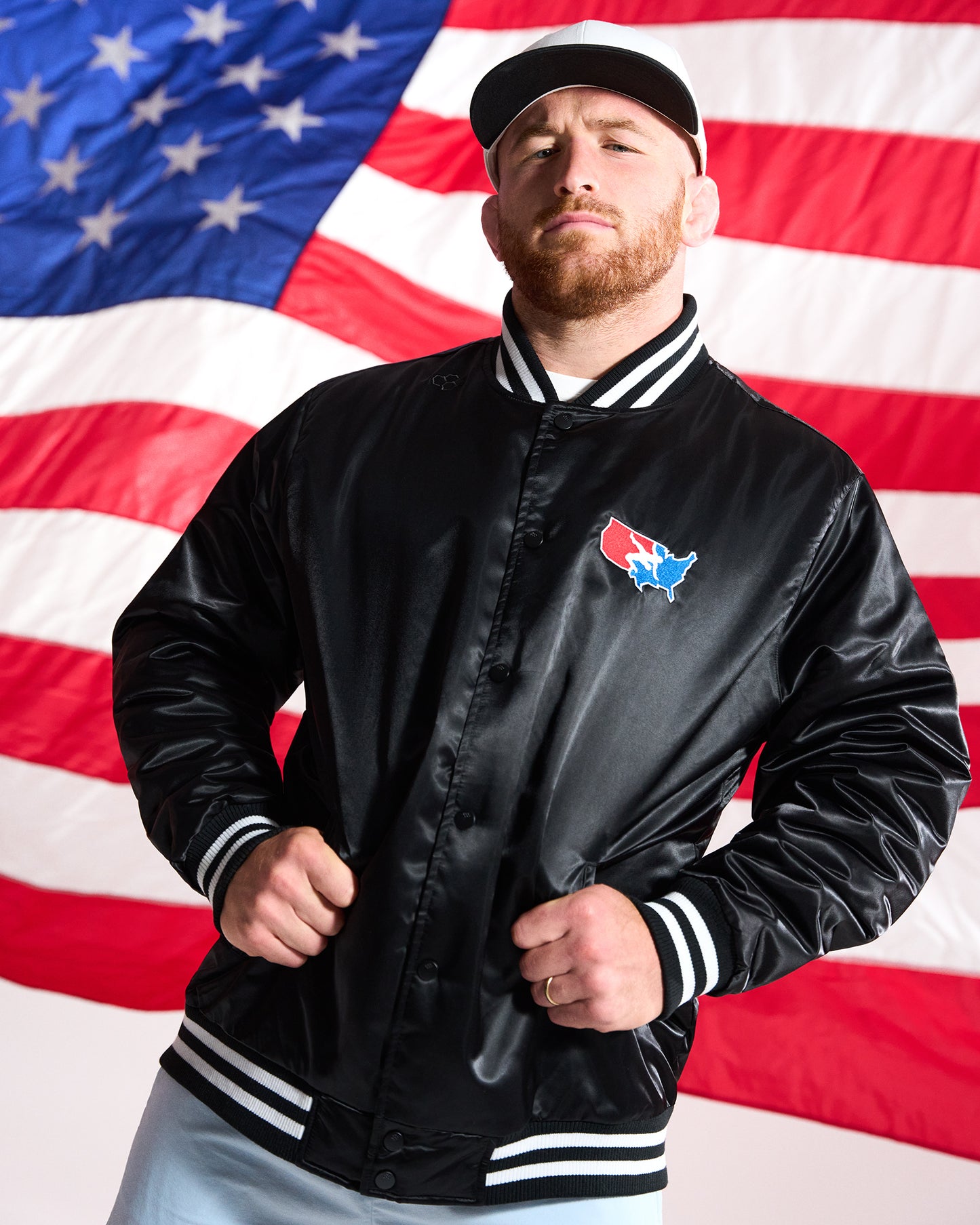 Man wearing a black satin jacket with a logo in front of an American flag