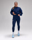 A woman modeling a matching navy blue activewear set consisting of a long-sleeve sweatshirt and high-waisted leggings, paired with white socks and light blue sneakers, against a neutral gray studio background.