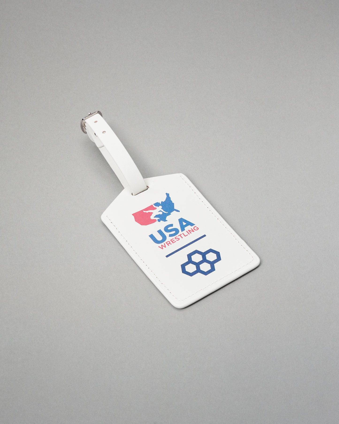 A white leather luggage tag with a silver metal buckle, featuring the USA Wrestling logo in red and blue on a gray background.