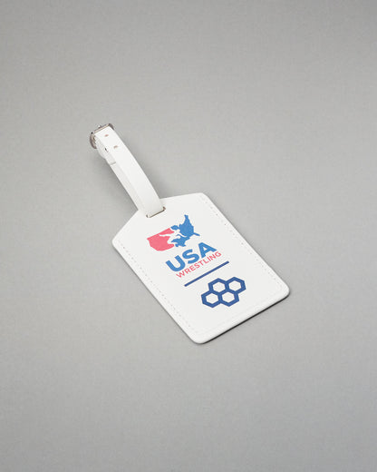 A white leather luggage tag with a silver metal buckle, featuring the USA Wrestling logo in red and blue on a gray background.