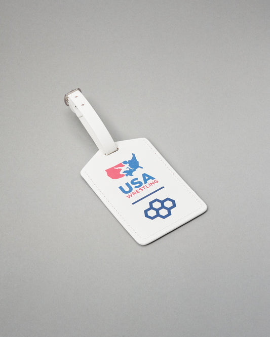 A white leather luggage tag with a silver metal buckle, featuring the USA Wrestling logo in red and blue on a gray background.