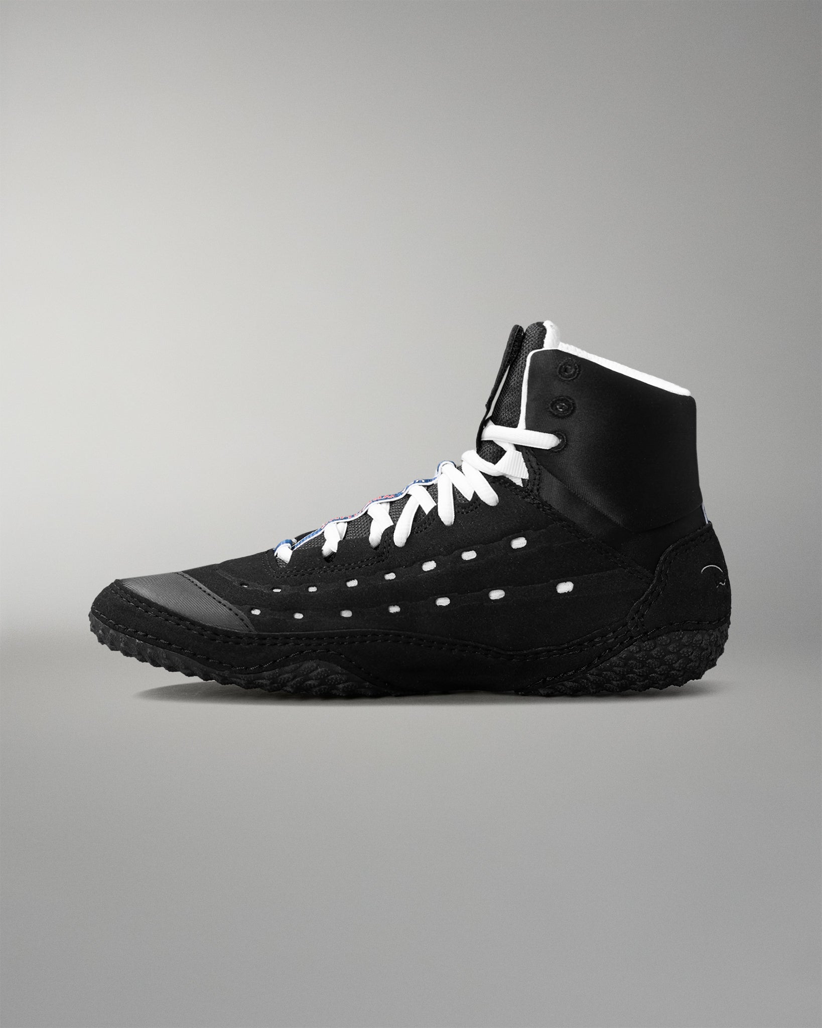 Black wrestling shoe with white laces on a gray background