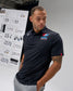 Man wearing a black polo shirt with a logo, standing in front of a display board.