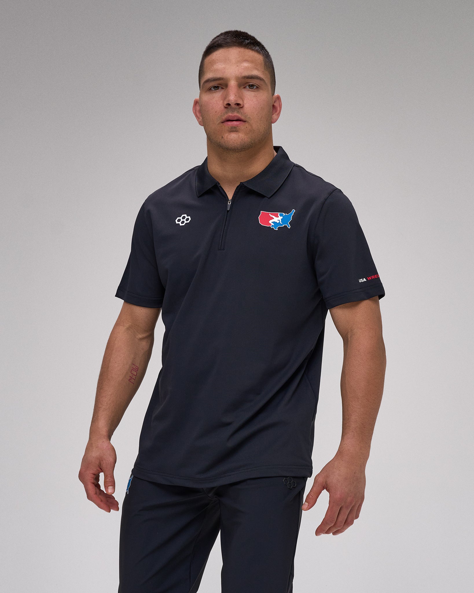 Man wearing a navy polo shirt with 'USA Wrestling' and 'RUDIS' logos on a gray background
