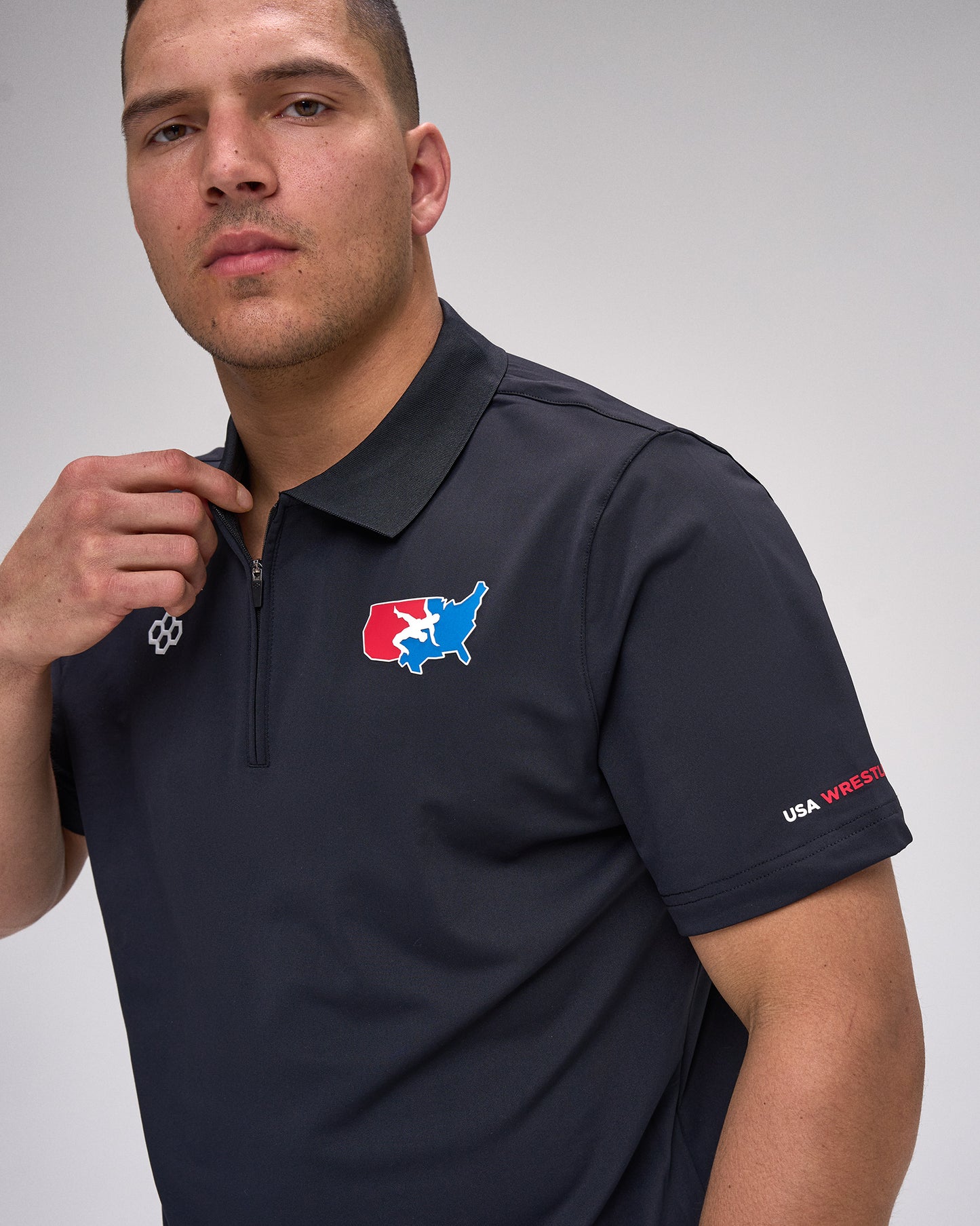 Man wearing a navy polo shirt with a 'USA Wrestling' logo and text on a gray background