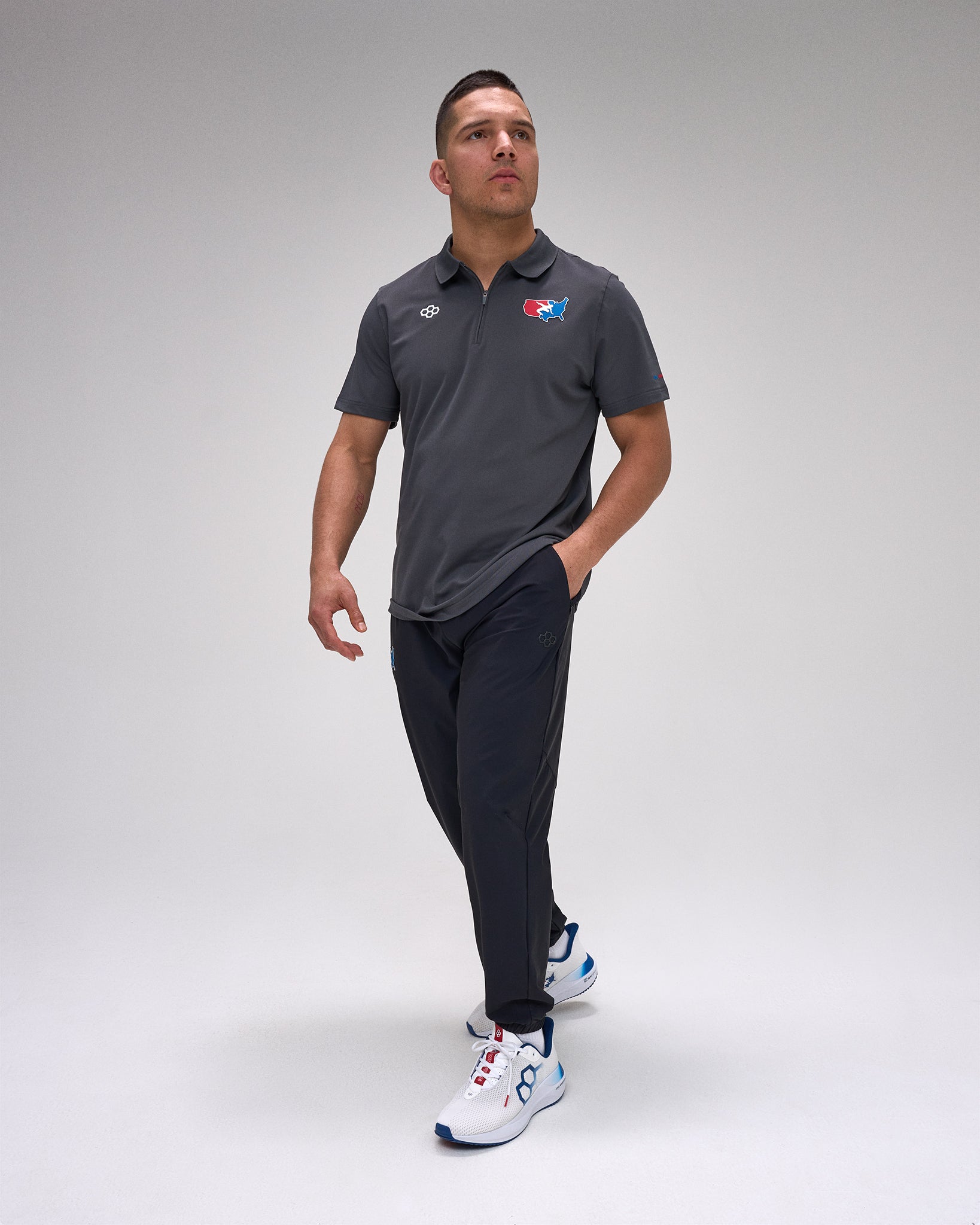 Man wearing a dark gray polo shirt with a 'USA Wrestling' logo and dark pants on a light gray background