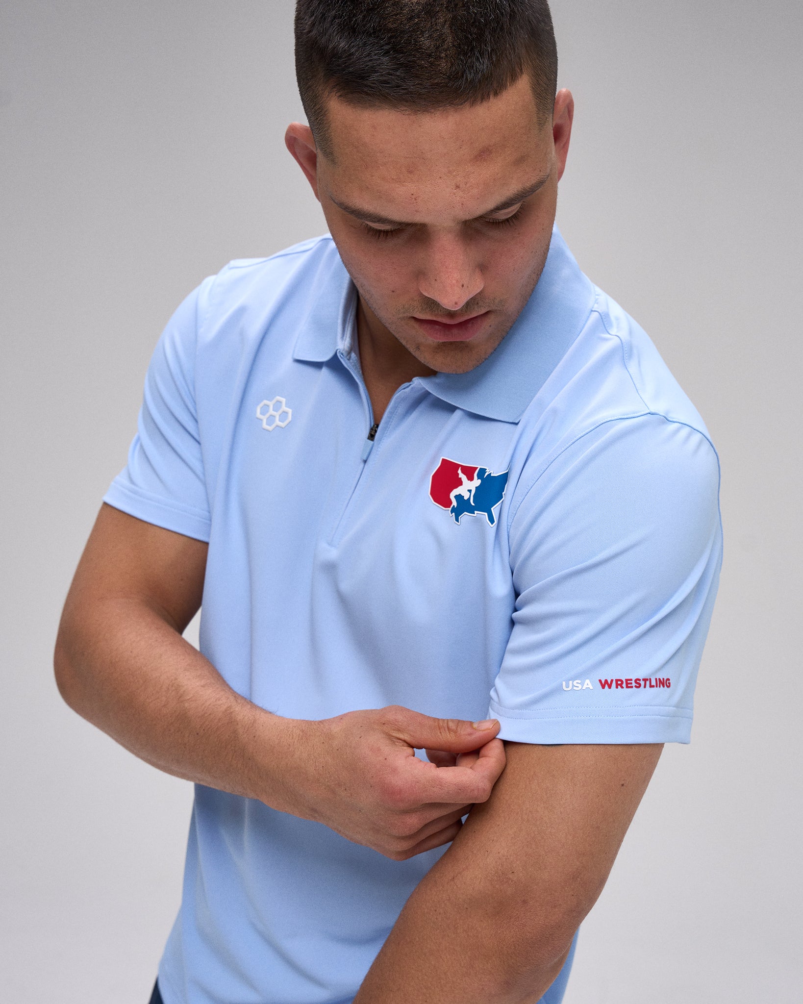 Man wearing a light blue polo shirt with 'USA Wrestling' logos on a gray background