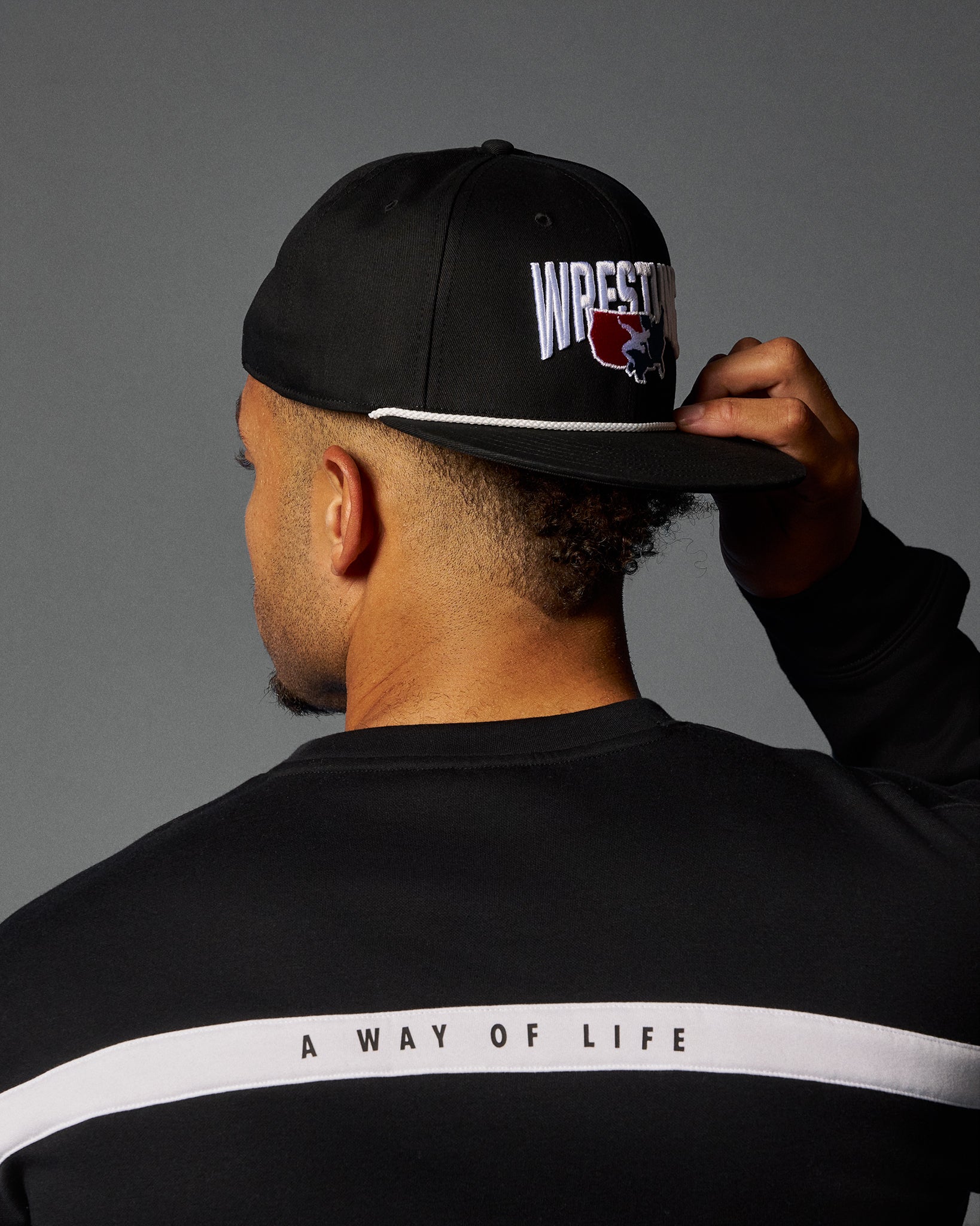 Person wearing a black cap with 'Wrestle' logo and black sweatshirt with 'A Way of Life' text.