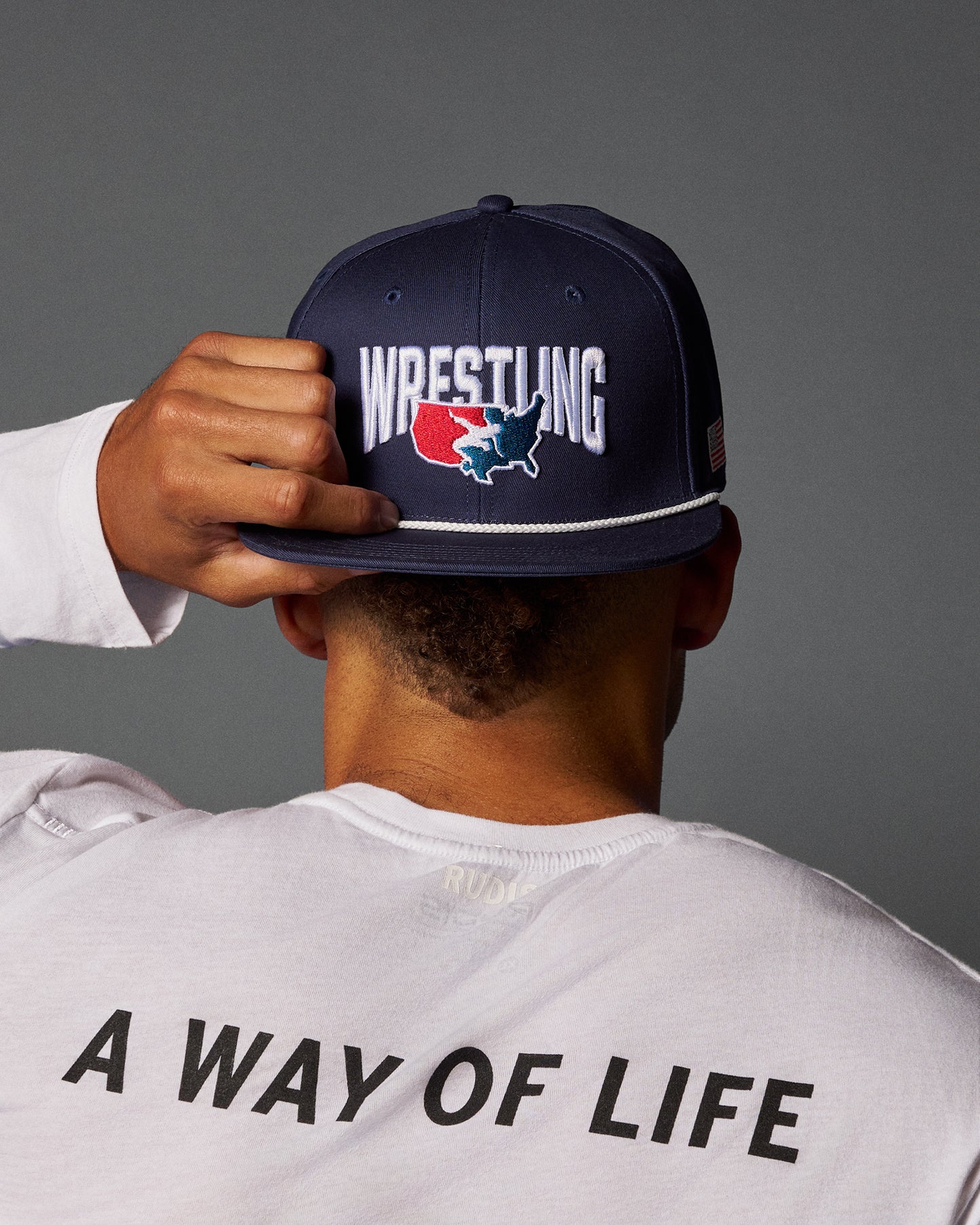 Person wearing a navy blue cap with 'Wrestling' printed on it, over a white shirt with 'A Way of Life' text.
