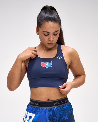 Woman wearing a navy sports bra with a logo and blue shorts on a white background