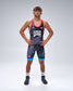 A male athlete stands with hands on hips wearing a USA wrestling singlet. The singlet is dark gray with a subtle pattern, featuring red trim, white 'USA' lettering on the chest, a small American flag, and bright blue accents on the shorts.