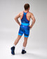 A man shown from the back wearing a blue USA wrestling singlet with red trim, blue and navy patterned shorts, white socks, and dark blue wrestling shoes against a light gray studio background.