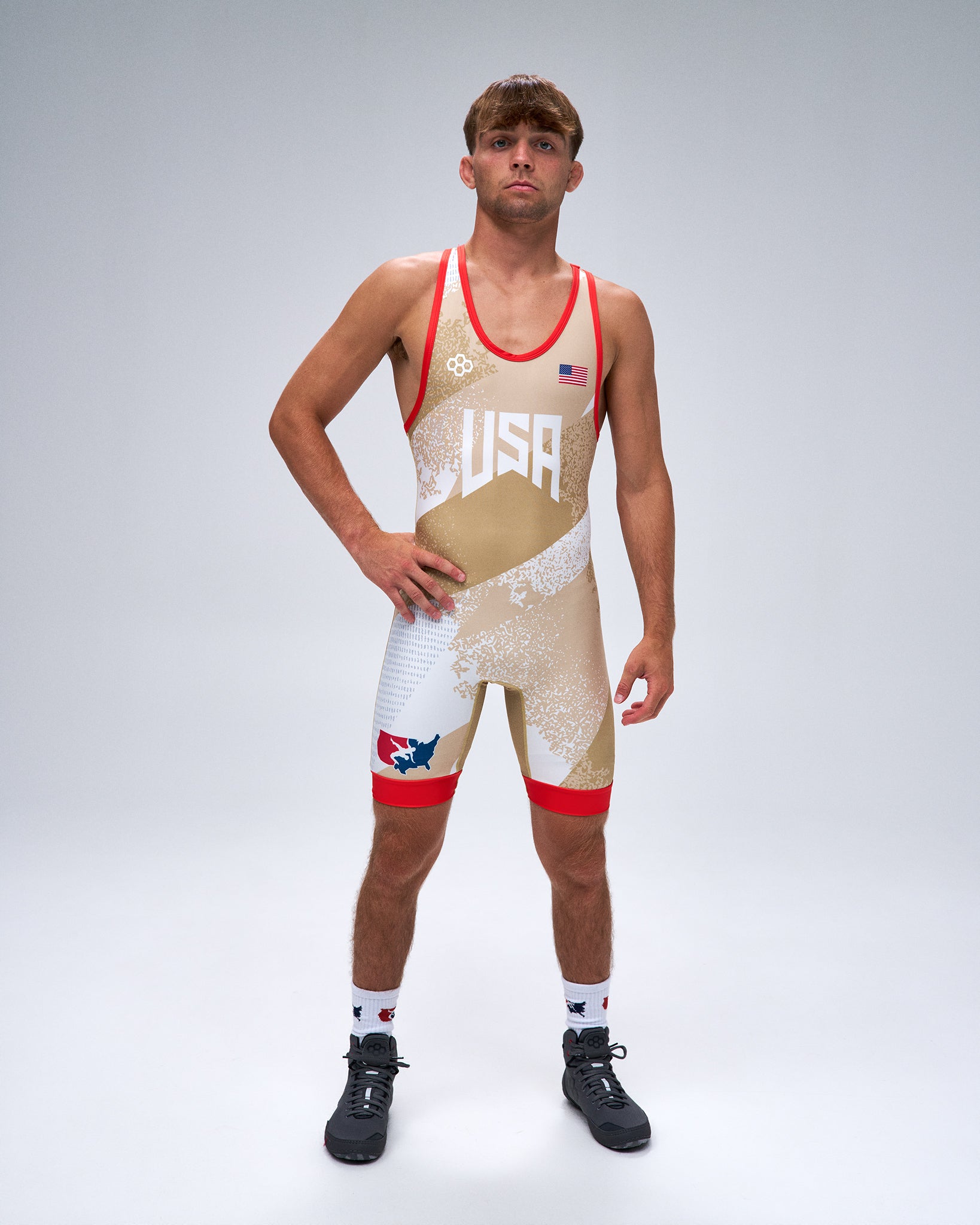 A male model wearing a USA Wrestling singlet in a gold, white, and red color scheme, standing against a light gray studio background.