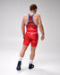 A male athlete shown from behind wearing a red and orange patterned wrestling singlet with blue trim, white USA lettering, and white socks, standing against a light gray studio background.