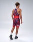 A man shown from the back wearing a red and navy USA Wrestling Singlet with a blue waistband and shoulder straps, paired with white socks and black shoes, against a light gray studio background.
