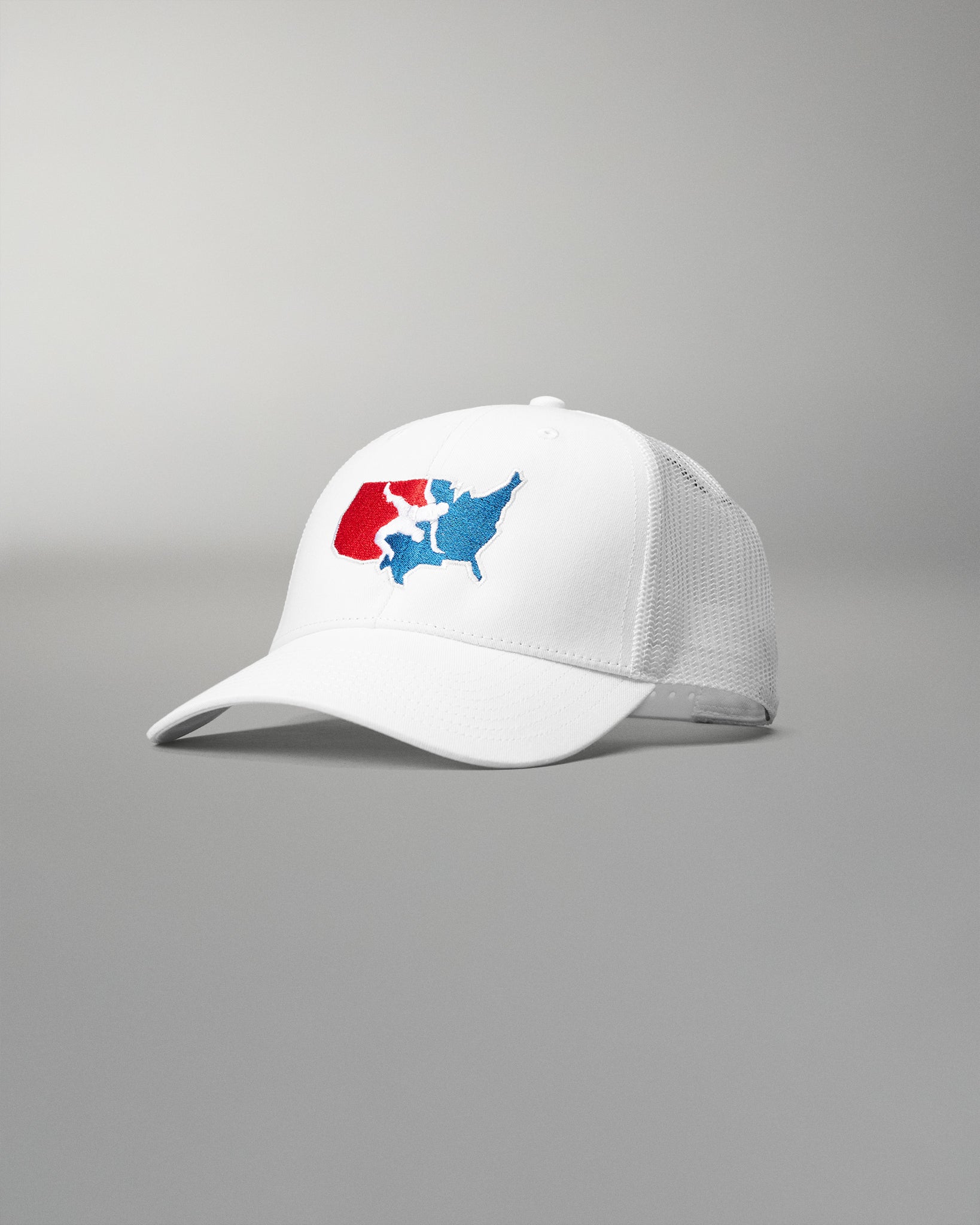 Front angled view of the RUDIS USA Wrestling Logo Bridge Trucker Hat in White, featuring an embroidered red, white and blue USA Wrestling logo, curved brim and white mesh panels.