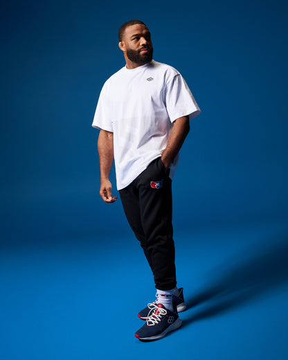 Man wearing a white t-shirt, black pants, and colorful sneakers on a blue background