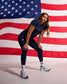 Female athlete wearing the RUDIS USA Wrestling Women's Navy Performance V-Neck T-Shirt, USA Wrestling leggings, and RUDIS training shoes poses in an athletic stance in front of an American flag.