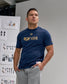 Man wearing a blue 'USA Wrestling' t-shirt standing in front of a wall with design boards.