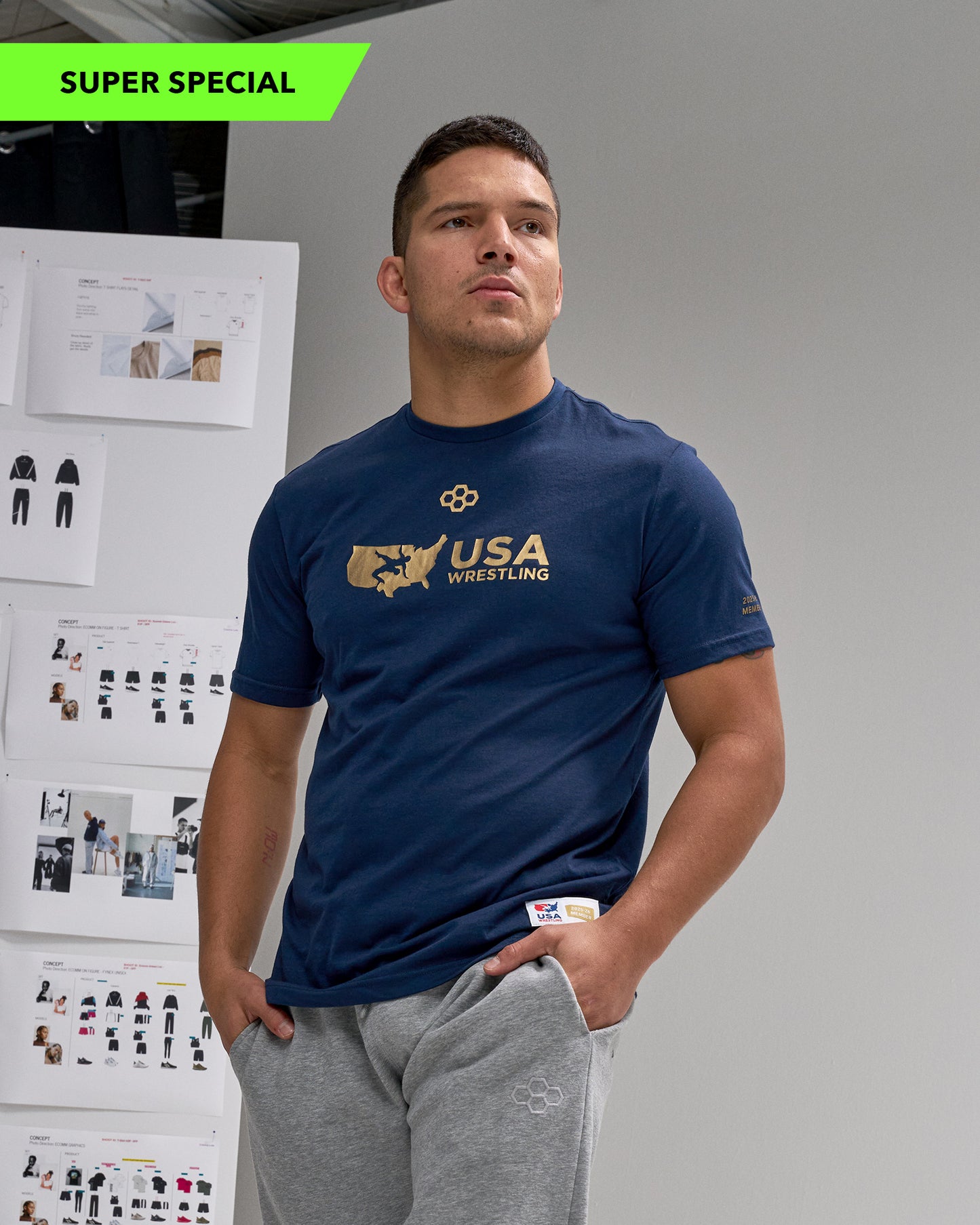 Man wearing a blue 'USA Wrestling' t-shirt standing in front of a wall with design boards.