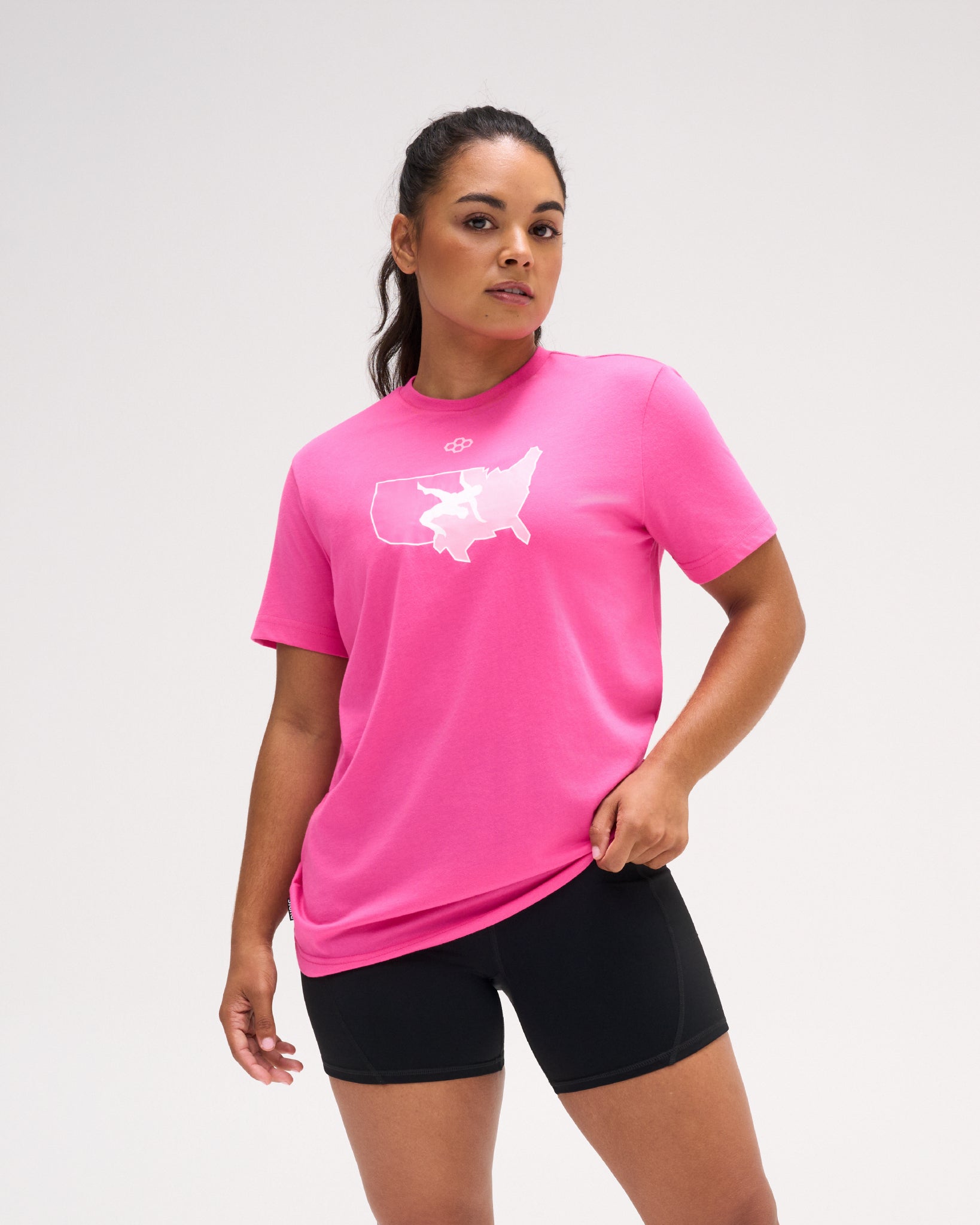 Woman wearing the pink RUDIS USA Wrestling Map Elite Super Soft T-Shirt with white USA wrestling map graphic and black athletic shorts.