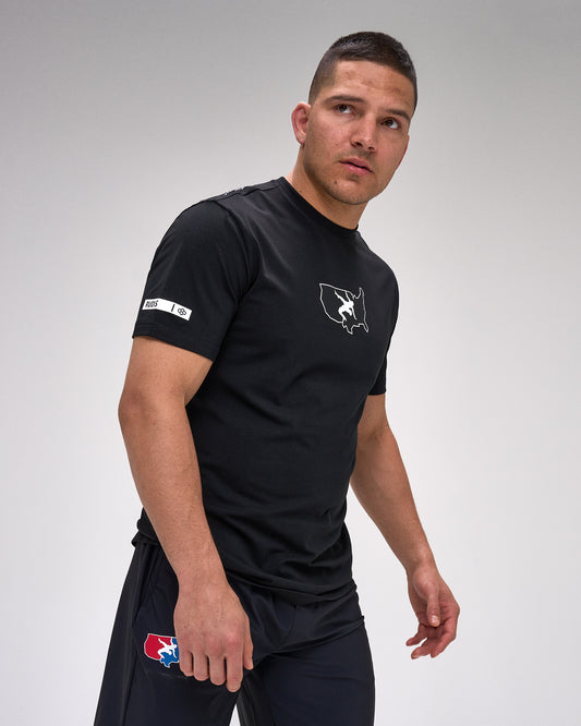 Man wearing a black athletic outfit with "USA Wrestling" and 'RUDIS' logos on a gray background