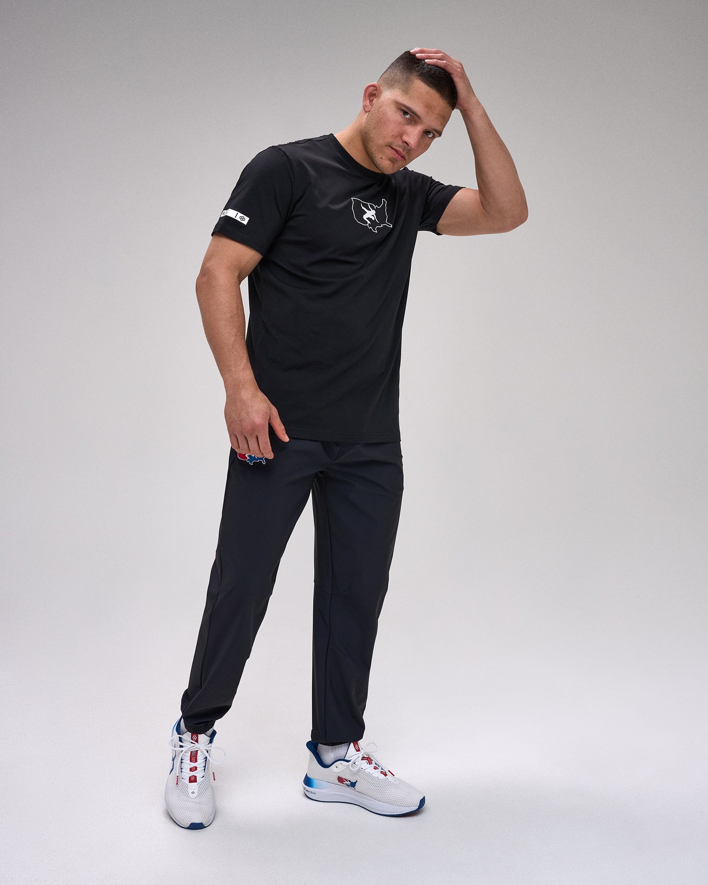 Man wearing a black t-shirt and pants with white sneakers on a gray background