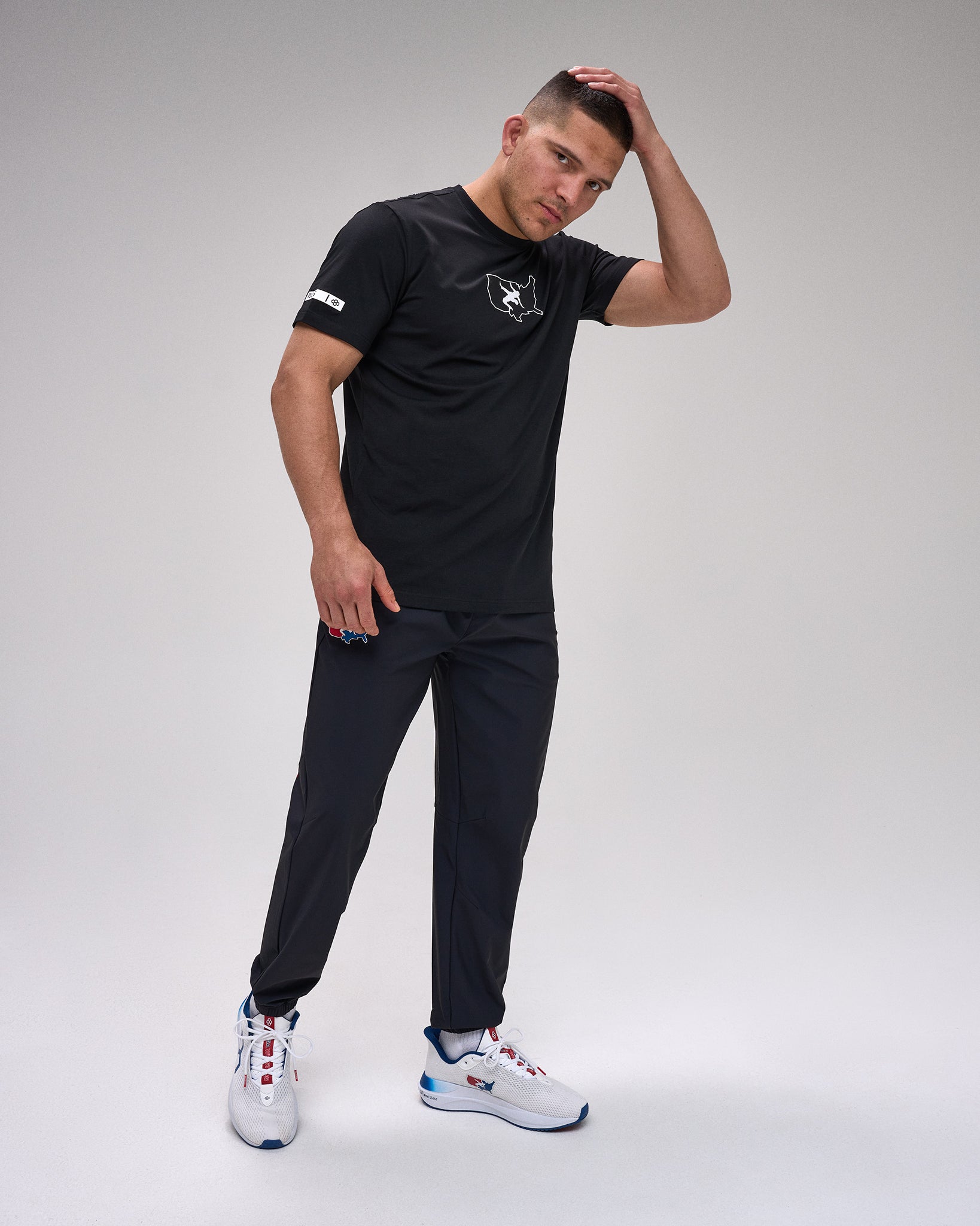 Man wearing a black t-shirt and pants with white sneakers on a gray background