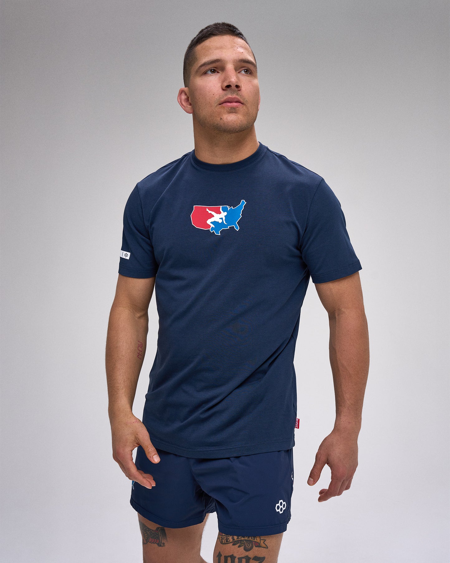 Man wearing a navy blue athletic outfit with a 'USA Wrestling' logo on a gray background