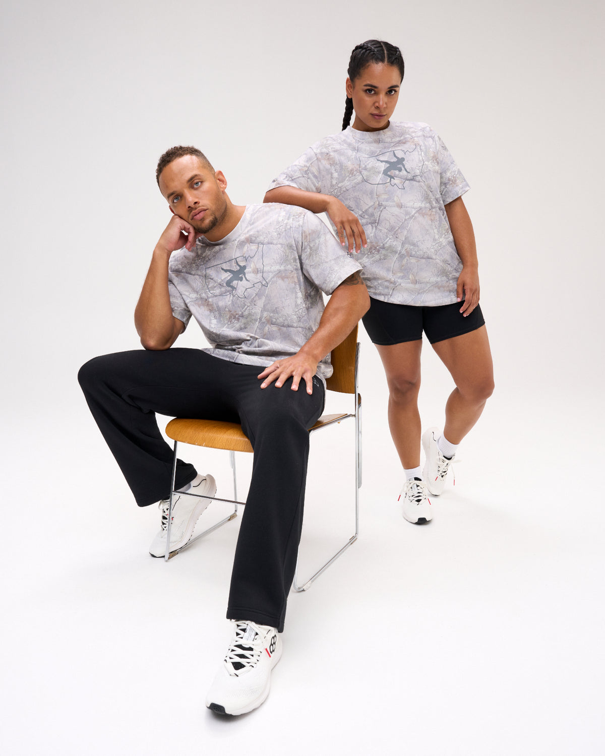 Male and female models wearing the USA Wrestling Map Classic Cotton T-Shirt in light gray tree camo with a USA map and wrestling graphic on the chest, paired with black athletic bottoms.