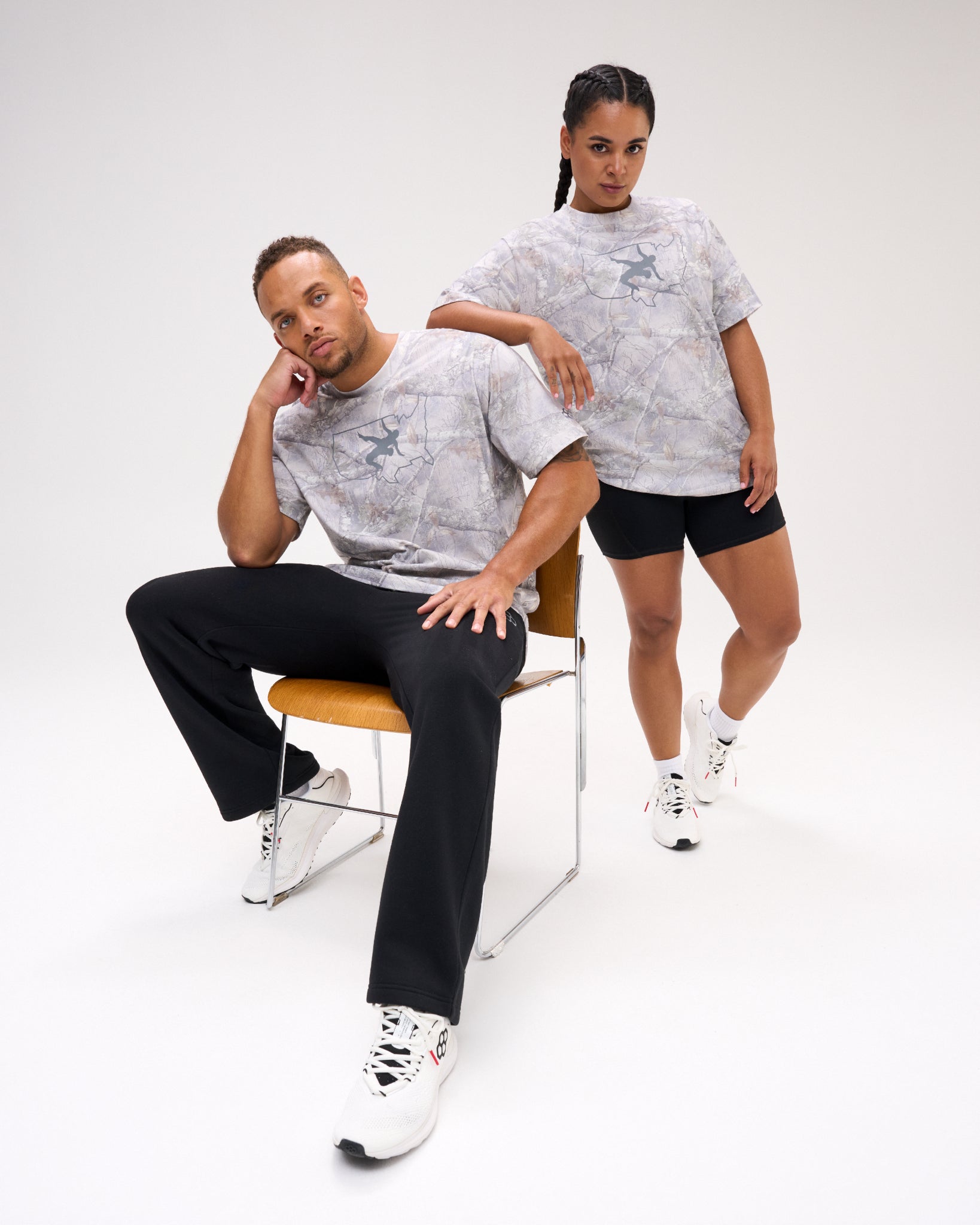 Male and female models wearing the USA Wrestling Map Classic Cotton T-Shirt in light gray tree camo with a USA map and wrestling graphic on the chest, paired with black athletic bottoms.