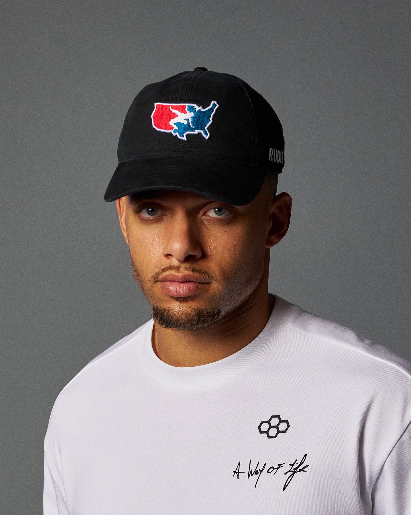 Man wearing a black cap with a logo and a white t-shirt with text on a gray background