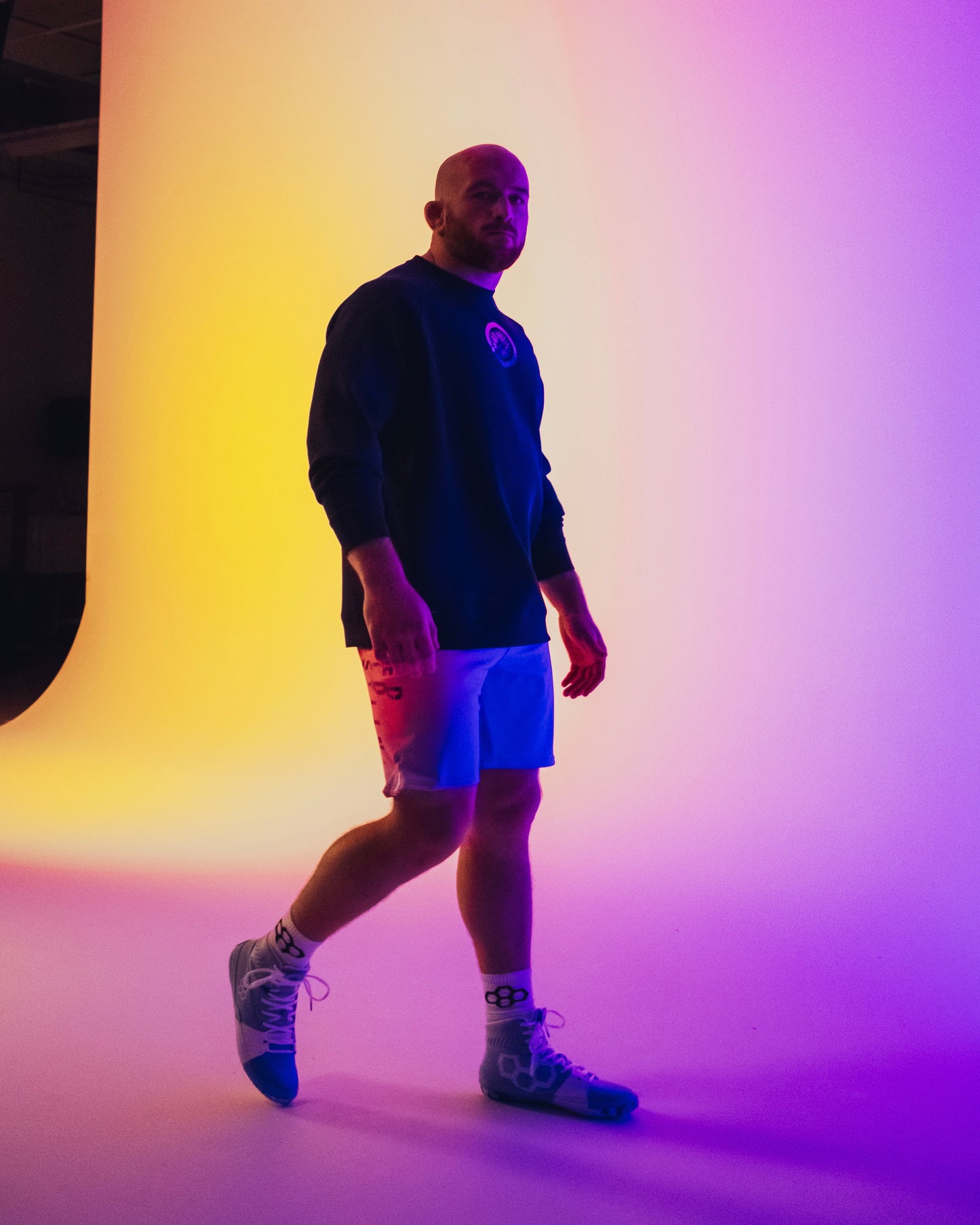 Person wearing a black hoodie and white shorts standing against a gradient wall.