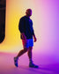 Person wearing a black hoodie and white shorts standing against a gradient wall.
