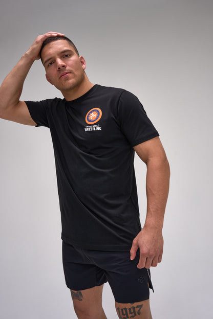 Man wearing a black t-shirt with a logo and black shorts on a gray background