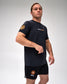 A man modeling a black athletic t-shirt and matching shorts set. The t-shirt features a yellow and orange logo on the left chest and a circular patch on the right sleeve.